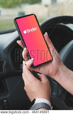Woman Holds A Smartphone With Tinder Dating App On Screen In Front Of The Steering Wheel Of A Car. T