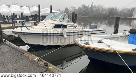 Moored Boats Tied In Their Boatslip With Shrink Wrapped Boats Stored For The Winter In The Backgroun