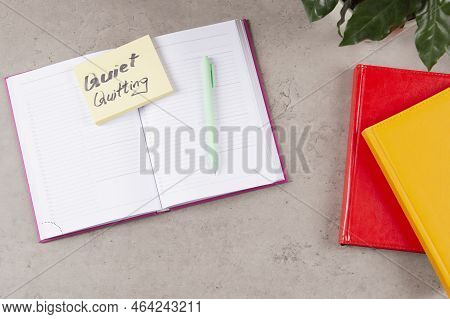 Workplace Desk With Paper Business Notebook Planner With Sticky Note And Text Quiet Quitting On It. 