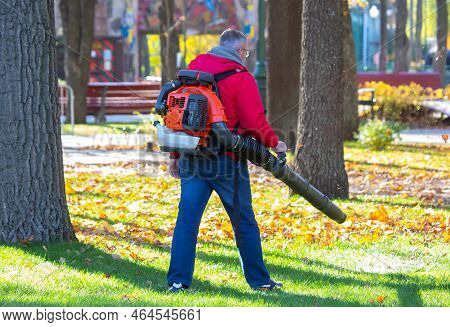 Worker Operating Heavy Duty Leaf Blower In City Park. Removing Fallen Leaves In Autumn. Park Cleanin