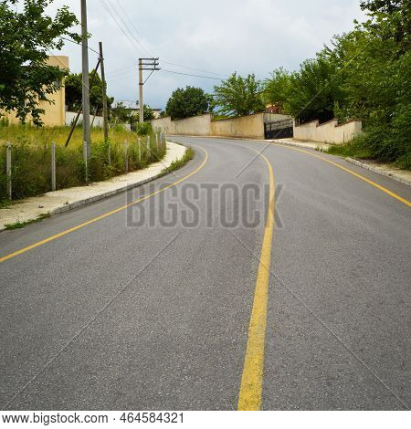 A Quiet Winding Town Road, Clean And Yellow Lined Asphalt Road, Winding Road Between Trees