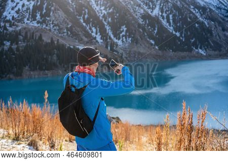 Warmly Dressed Man Taking A Picture With His Phone Of The Stuningly Beautiful Lake Surrounded By Sno