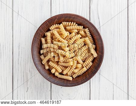 Uncooked Fusilli Pasta In Ceramic Bowl On White Wooden Background