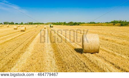 Above View Round Bale Of Straw After Harvest, In Background Tractor Is Pulling Round Baler, Machine 