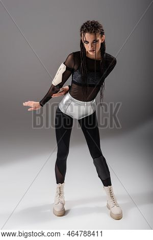 Full Length Of Futuristic Woman In Black Bodycon Jumpsuit And Silver Shorts On Grey Background.