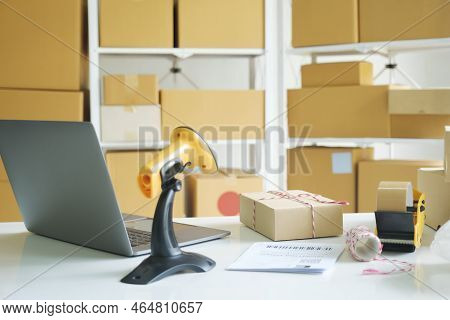 Photograph Of Online Business Quipments Including Laptop, Cardboard Boxes, Scanner, Tying Rope, Pape