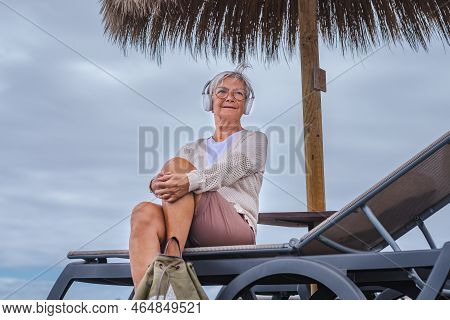 Portrait Of Attractive Senior Woman Wearing Eyeglasses And Headphones Listening Music Sitting At The