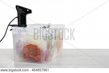 Sous Vide Cooker And Vacuum Packed Food Products In Box On Wooden Table Against White Background, Sp