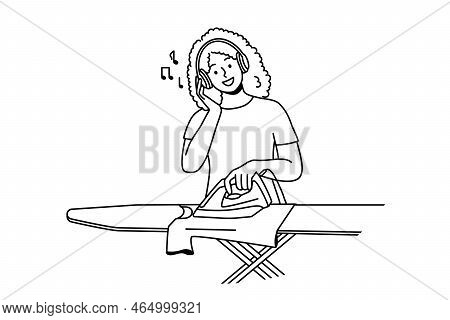Smiling Young Woman In Headphones Ironing Clothes At Home. Happy African American Girl Listen To Mus