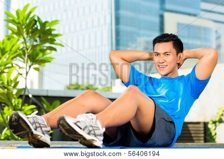 Urban Sport - junger asiatischer indonesischer Mann aufwärmen und Sit-ups macht vor der Ausführung in der Stadt