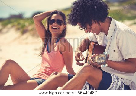 Cute hispanic couple playing guitar serenading on beach in love and embrace