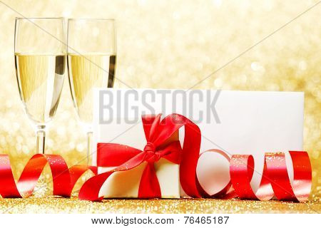 Champagne glasses and present in whitebox with red ribbon on golden background