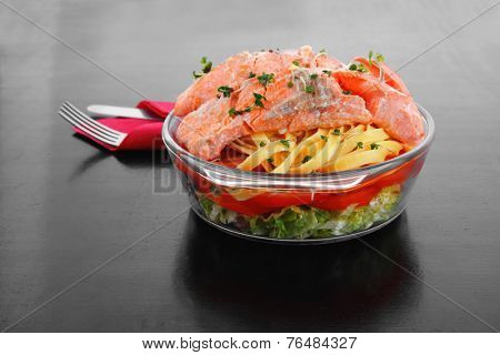 fresh fried natural pink salmon on italian traditional tagliatelle backed with tomato and vegetables served over black wooden table