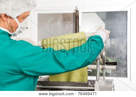 Cropped image of male chef unwrapping pasta sheet from rolling pin into machine at commercial kitchen