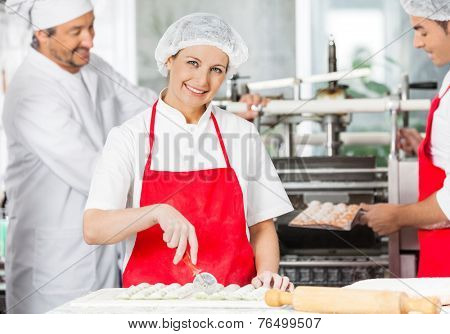Portrait of happy female chef preparing ravioli pasta at counter with colleagues working in background at commercial kitchen