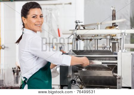 Portrait of happy female chef processing ravioli pasta in machine at commercial kitchen