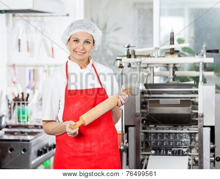Portrait of smiling female chef holding rolling pin in commercial kitchen