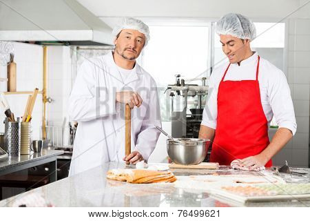 Portrait of confident male chef standing with colleague preparing ravioli pasta at commercial kitchen counter