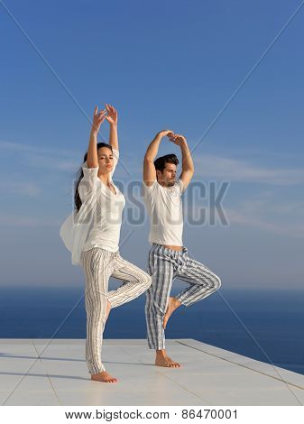 young couple practicing yoga at sunset in modern home terace with ocean and sunset in background