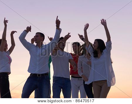 group of happy young people dancing and have fun on party in modern home bacony with sunset and ocean in background