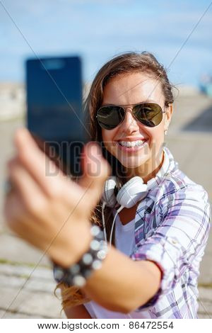 holidays and tourism concept - smiling teenage girl taking picture with smartphone camera aoutdoors