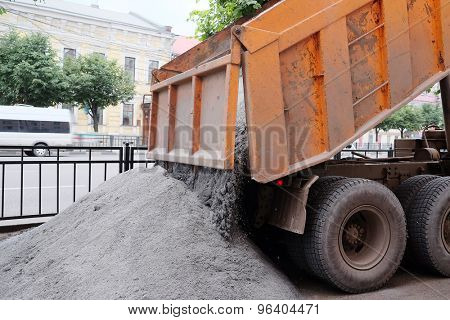 The dump truck pours out cement on the repaired sidewalk