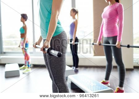 fitness, sport, people and lifestyle concept - close up of women exercising with bars and step platforms in gym
