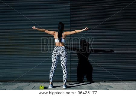 Back view portrait sporty woman with perfect figure and buttocks stretching her arms against wall