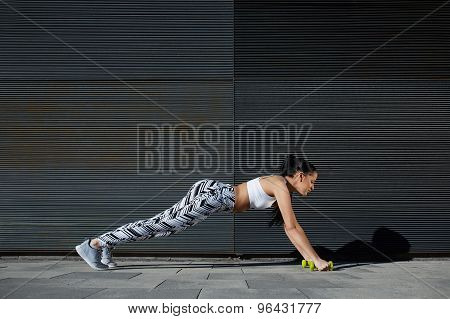 Healthy young female in workout gear doing push-ups on black background outdoors