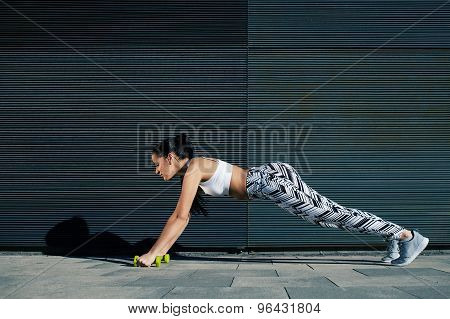 Female in workout gear doing push-ups with some weights against wall with copy space for your text