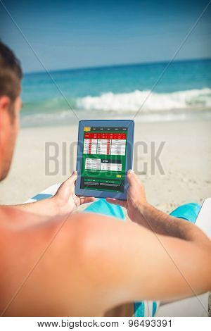 Man using digital tablet on deck chair at the beach against gambling app