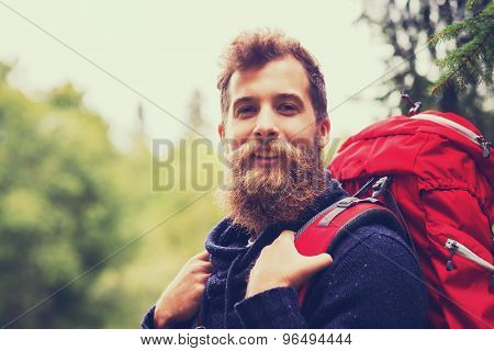 adventure, travel, tourism, hike and people concept - smiling man with beard and red backpack hiking