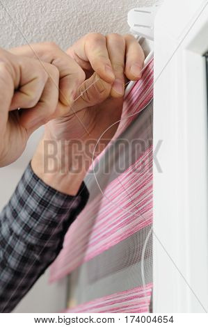 Installing fabric roller blinds. A man pulling the rope that guides the movement of roller blinds.