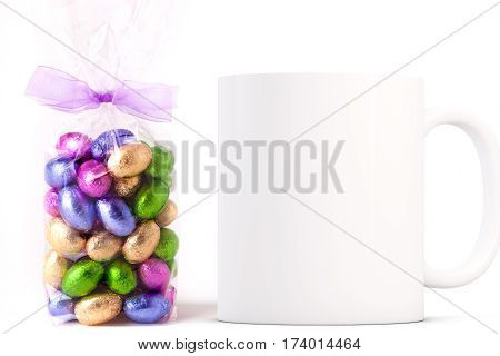 Easter Mug Mockup. Coffee mug mockup next to a cellophane wrapped bag of gold wrapped chocolate mini eggs. Perfect for Easter mugs.