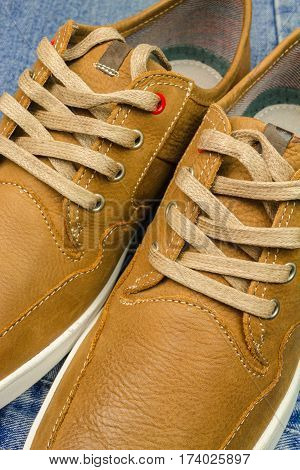 Pair of tan color leather sneakers on jeans background close-up view