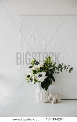 Elegant bouquet of anemones in a vase on table in white room interior, floral home dcoration