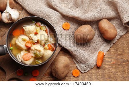 Stewpan with delicious chicken and dumplings on wooden background