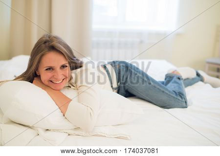 Smiling thoughtful pretty woman lying in bed at home.