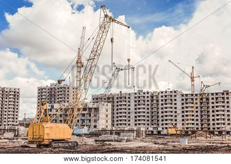 Construction area with the building machinery and incomplete skycrapers against a hard sky background.