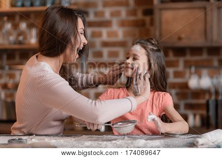 'Happy mother and daughter having fun while sifting flour at kitchen