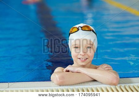 Portrait of cute energetic kid smiling to camera at border of pool during swimming lesson