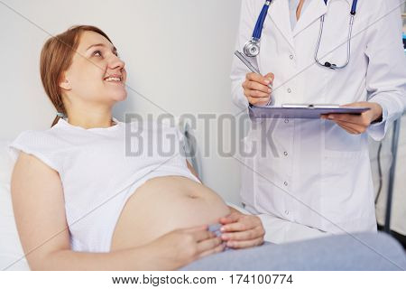 Close-up view of pregnant woman lying in clinic on check-up, getting good news from doctor and smiling cheerfully
