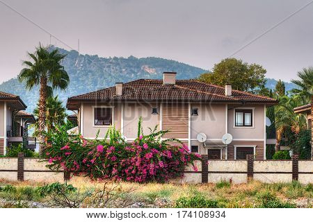 Camyuva Kemer Antalya Turkey - 28 august 2014: two-storey villa surrounded by palm trees and flowering bushes against the backdrop of forested mountains in the village of Camyuva Resort.