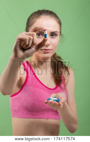 Young girl at gym showing pills. Shallow depth of field. Focus on pill.