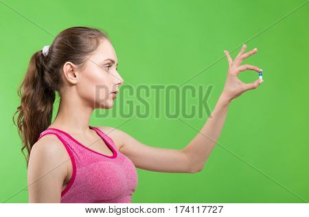Young girl at gym showing pills on green background