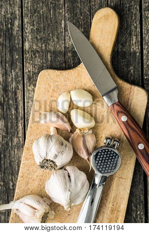 Garlic and garlic press on cutting board and knife. Top view.
