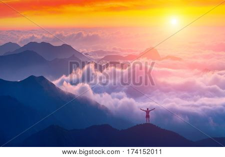 Man standing on a mountain top with rised hands and welcome sunrise in a Crimea mountains above the cloudy valley