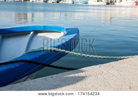 Stern of a blue fishing boat docked in port tied with mooring lines waterfront sunny day closeup yachts in the background