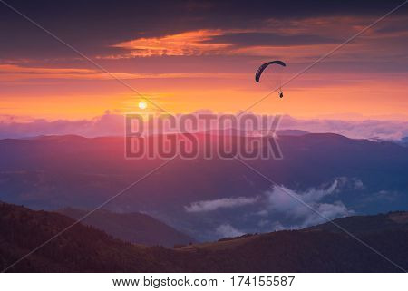 Paraglide silhouette against the sunset sky flying over the mountain valley.