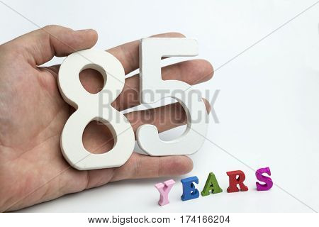 Hand holding number eighty-five on a white background.